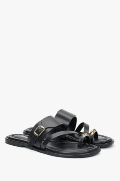 Czarne skórzane klapki Estro z pętelką na palec, eksponujące asymetryczną linię cholewki oraz wyrazistą złotą klamrę.